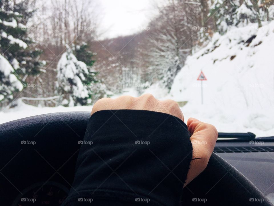 Hand on the steering wheel with snowy scenery seem through the windshield 