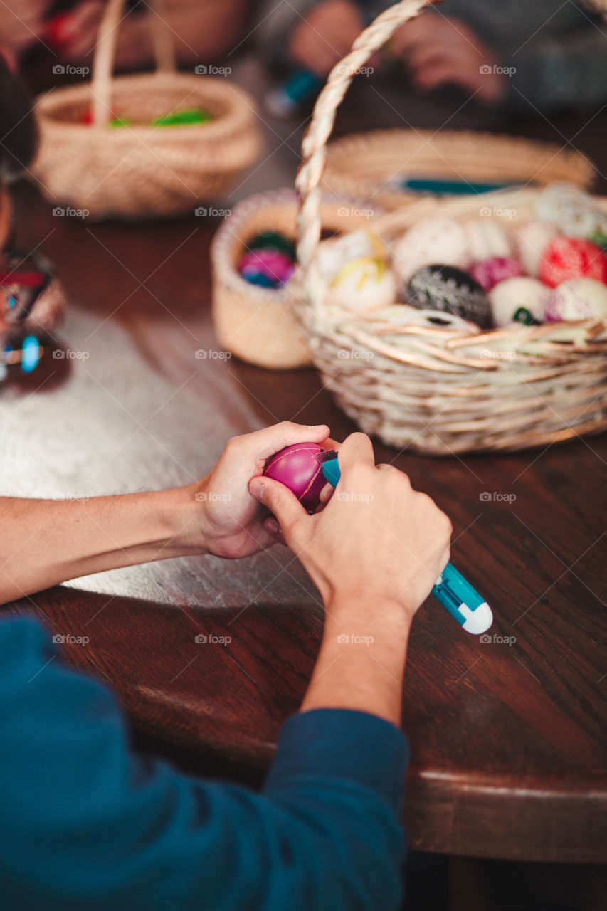 Man decorating the Easter eggs by scratching patterns on dyed eggs. Traditional Easter time, spring time, new beginnings. Candid people, real moments, authentic situations