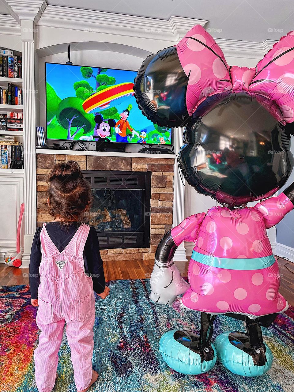 Toddler girl standing with Minnie Mouse balloon, toddler watching tv with Minnie Mouse, toddler girl wearing pink, Minnie Mouse and toddler girl watching Mickey Mouse tv show, toddler girl loves Minnie Mouse