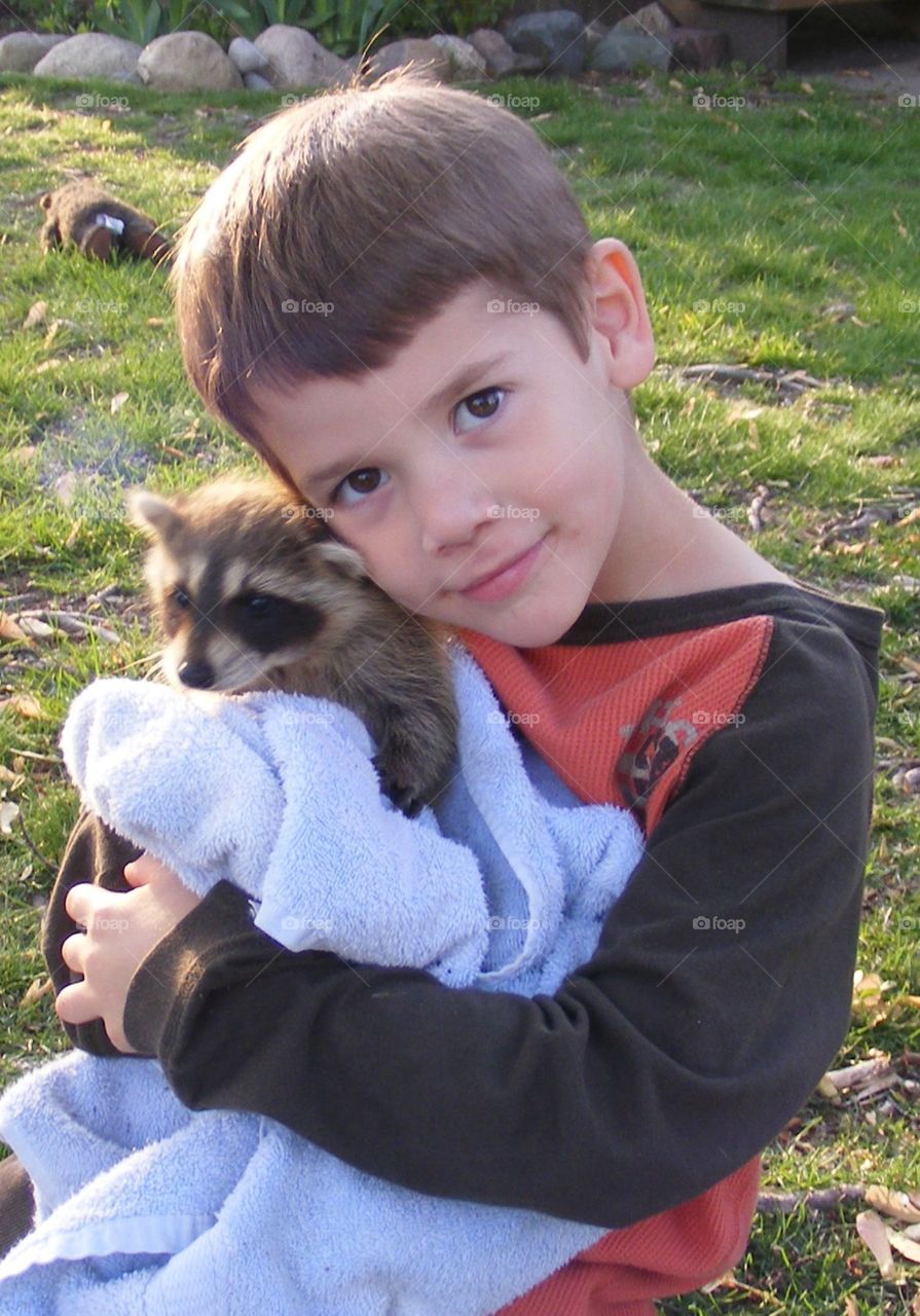 Boy hugging baby raccoon