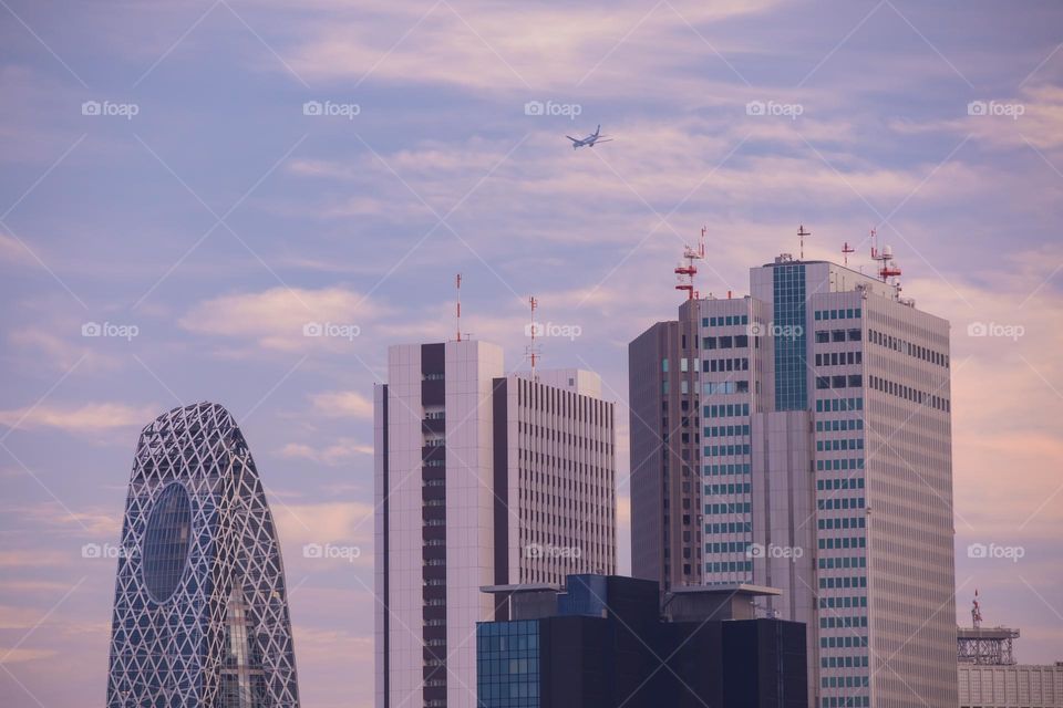 Closeup up of the top of skyscrapers in Shinjuku. One of the most crowded places in Tokyo, Japan where businesses and residences gather. An ANA (All Nippon Airways) airplane flies above at sunset.