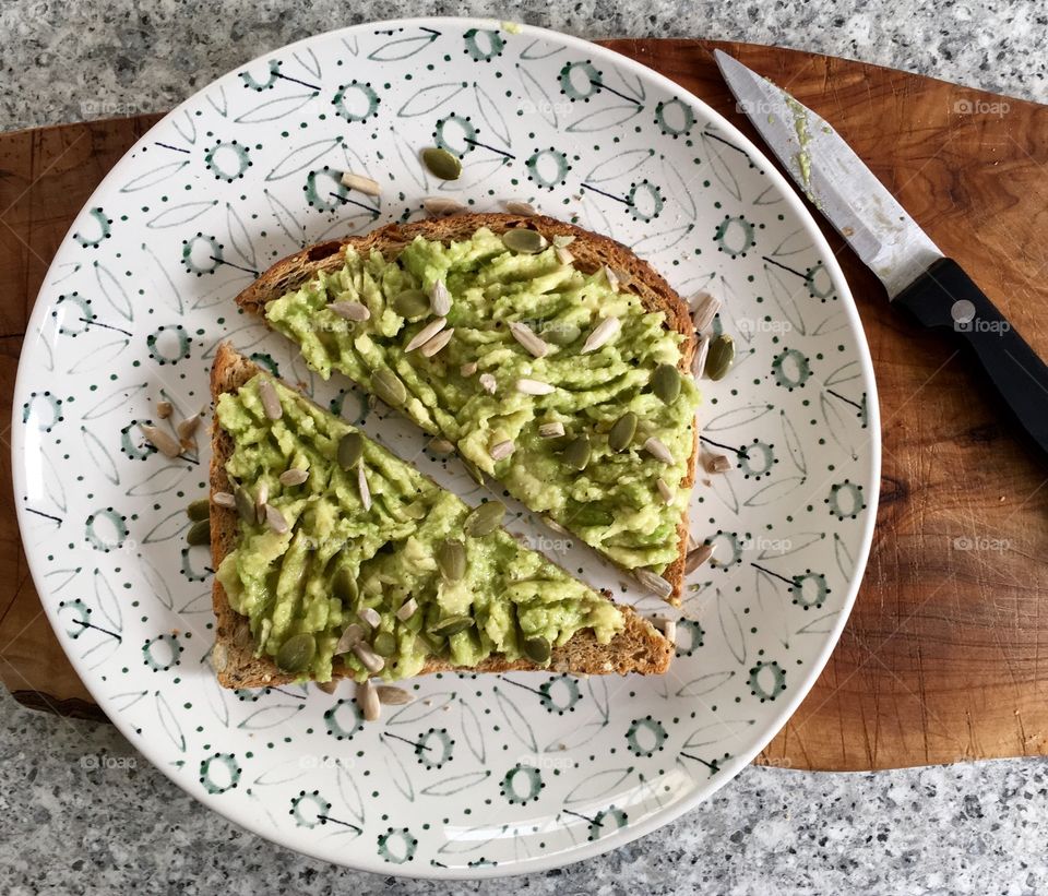 Avocado toast on seeded bread scattered with pumpkin and sunflower seeds and drizzled with olive oil