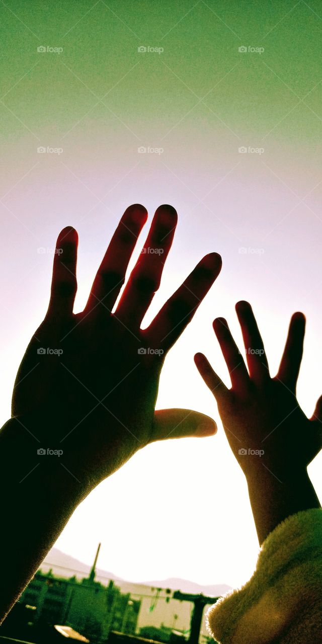 The silhouettes of both hands of mother and daughter against the bright light from the sunrise.