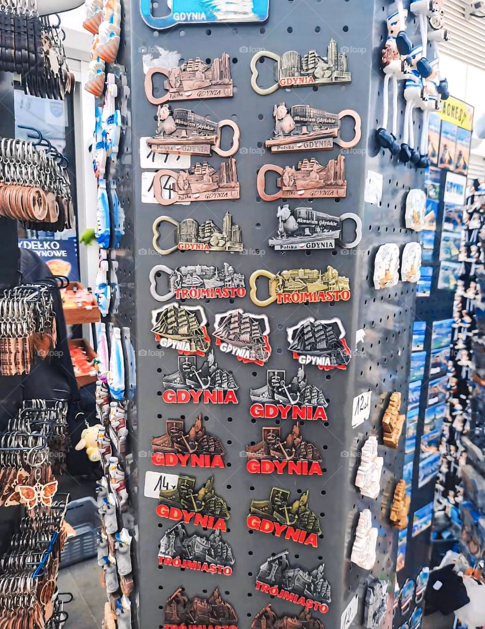 A colorful display of souvenir magnets and bottle openers featuring "Gdynia" and "Trójmiasto" designs, showcasing iconic Polish landmarks, perfect for collectors and tourists visiting Poland.