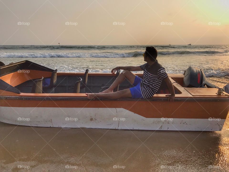 Man posing in boat at beach during sunset