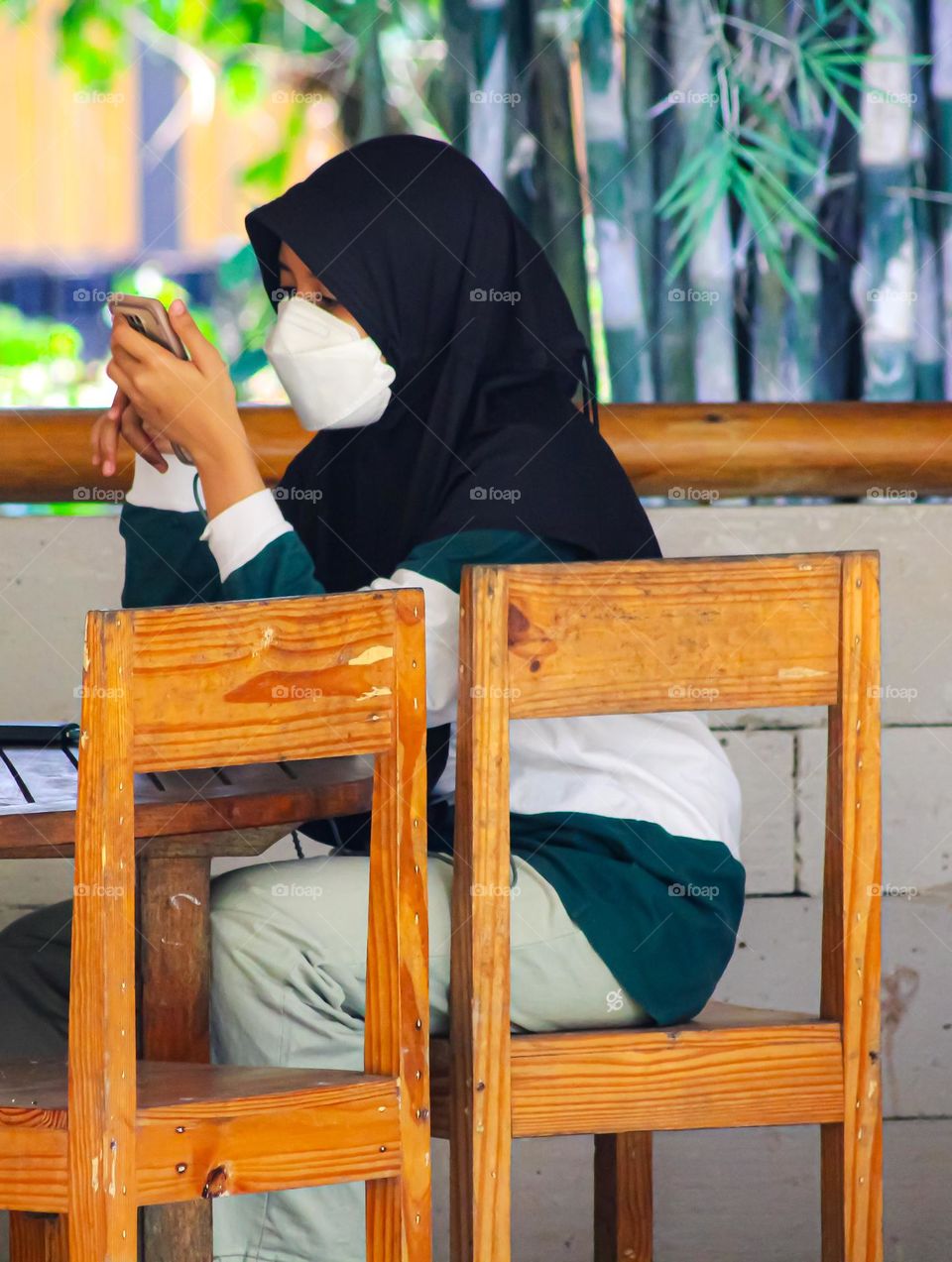 A girl wearing a mask is sitting and playing with her cellphone.