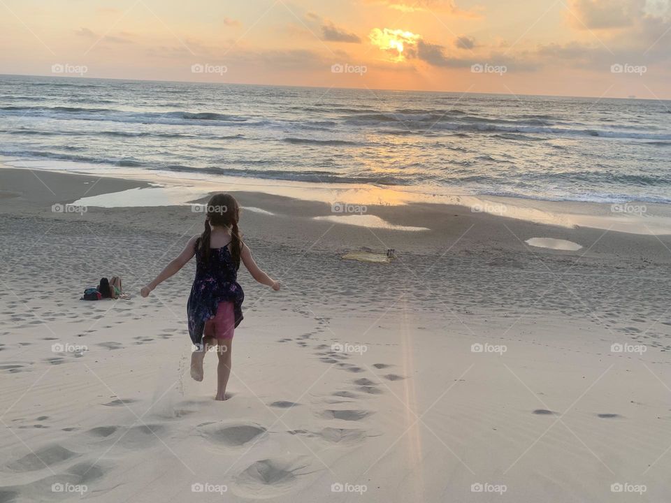 Girl running down the sand dune on the beach at sunset 