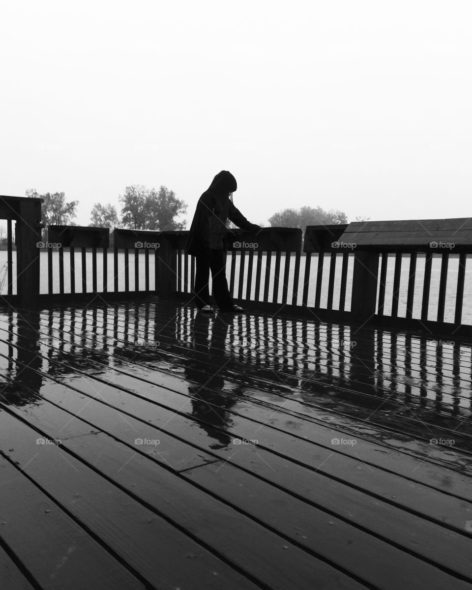 Girl standing alone in rain on pier with reflection 