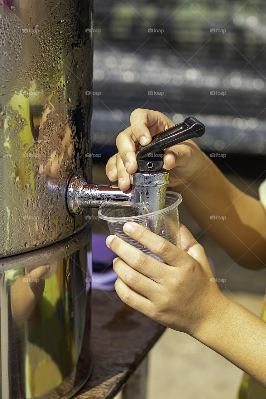 Hand boy holding the glass with water from the water cooler.