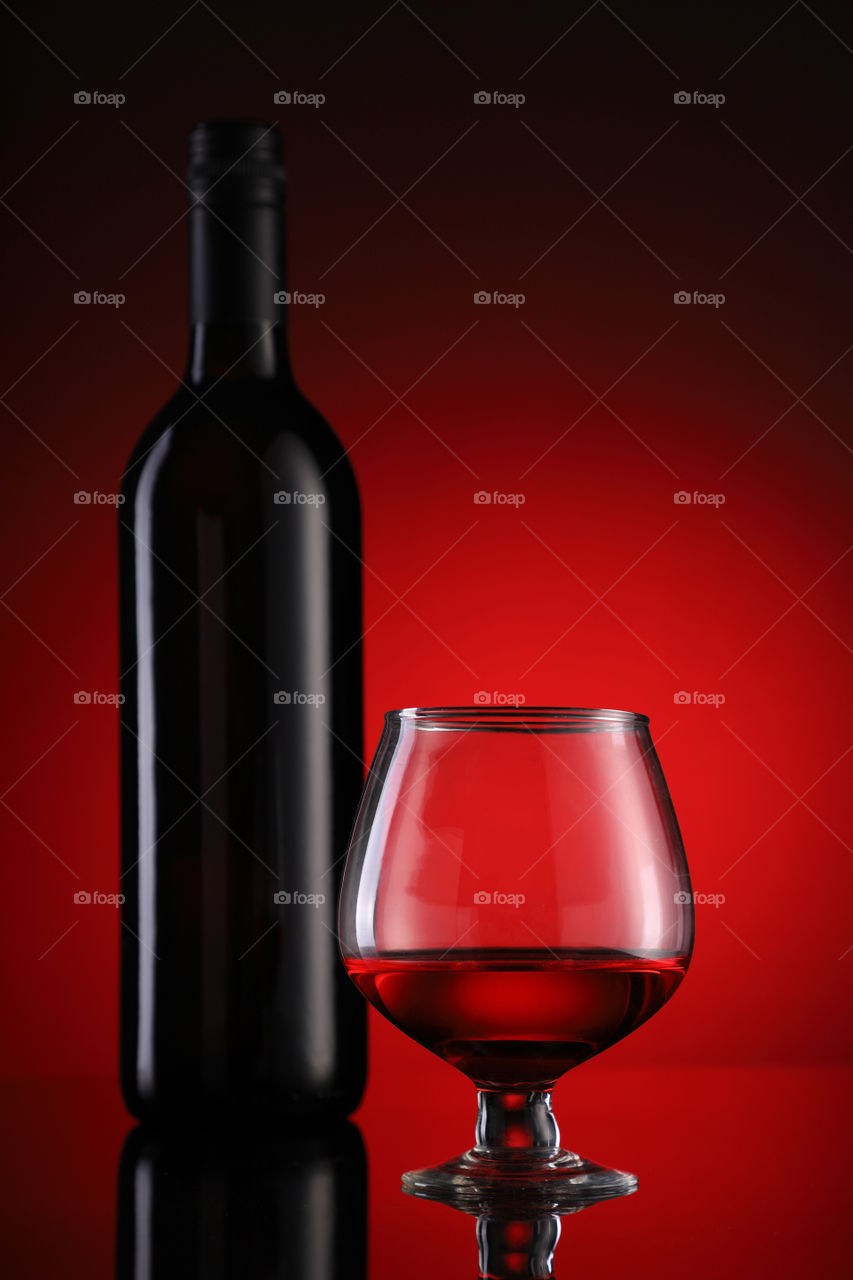 Red wine glass and bottle on red background