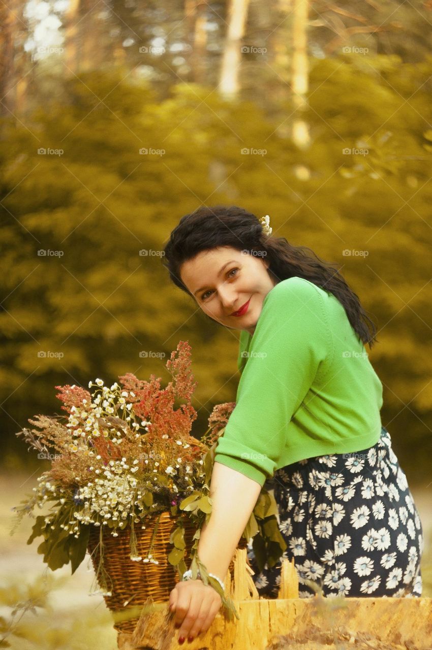 portrait of a mother in a green forest with a basket of flowers