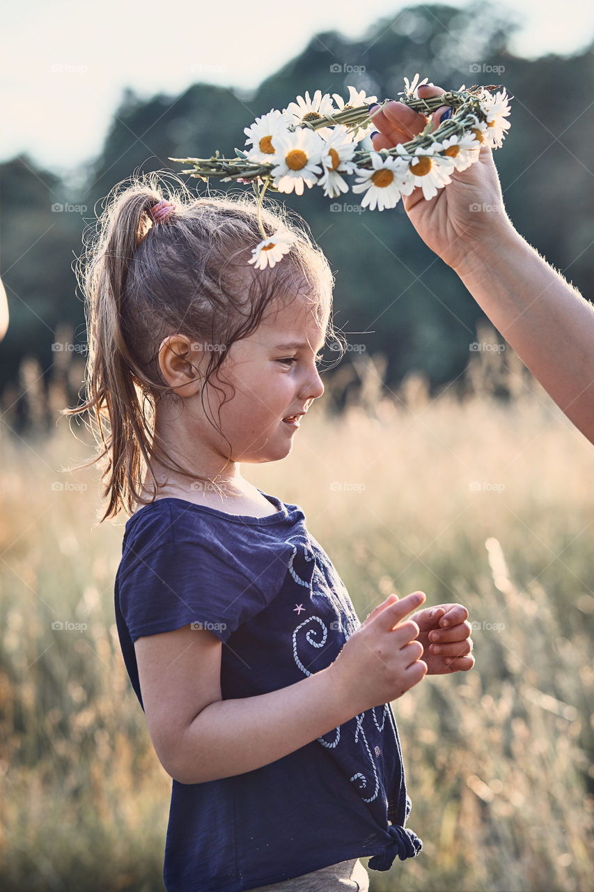 Mother putting a coronet of wild flowers on a head of little girl. Family spending time together on a meadow, close to nature. Parents and children playing together. Candid people, real moments, authentic situations