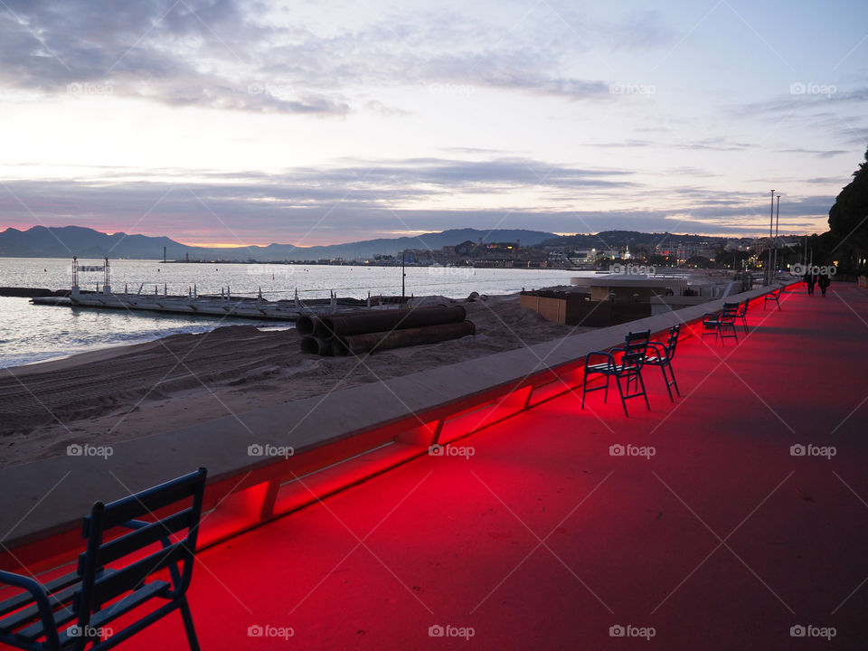 Blue chairs and red lighting on the Croisette in Cannes, France on an beautiful evening.