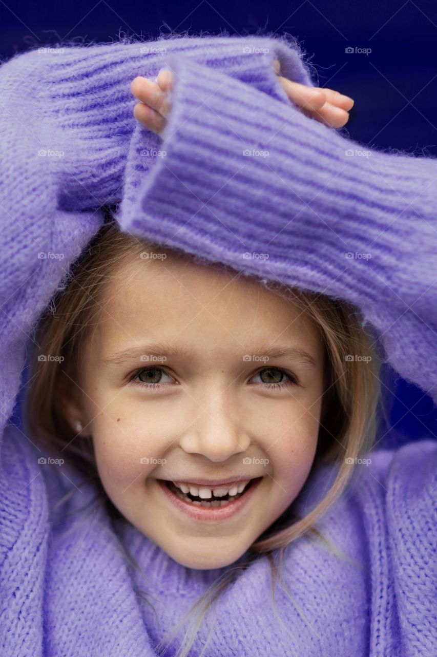 Portrait of cute Caucasian little girl with blonde hair wearing violet sweater 