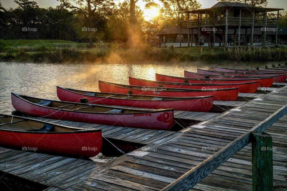 Foap, Art of Composition. A touch of fog remains over the pond as the sun rises with a row of red canoes ready to entertain guests at Camp Seafarer in Arapaho North Carolina. 