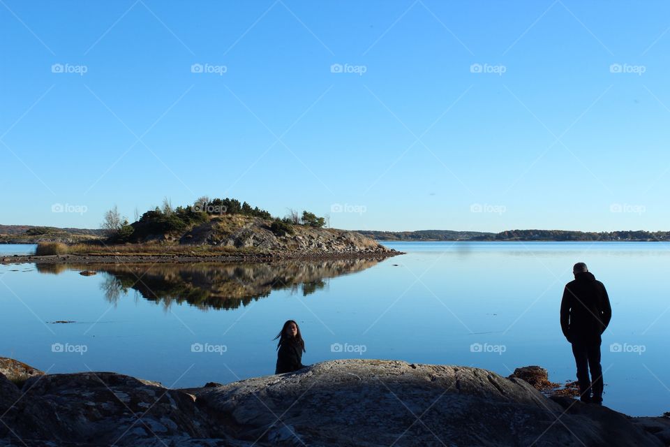 Blue sky and water, two persons on a rocky beach