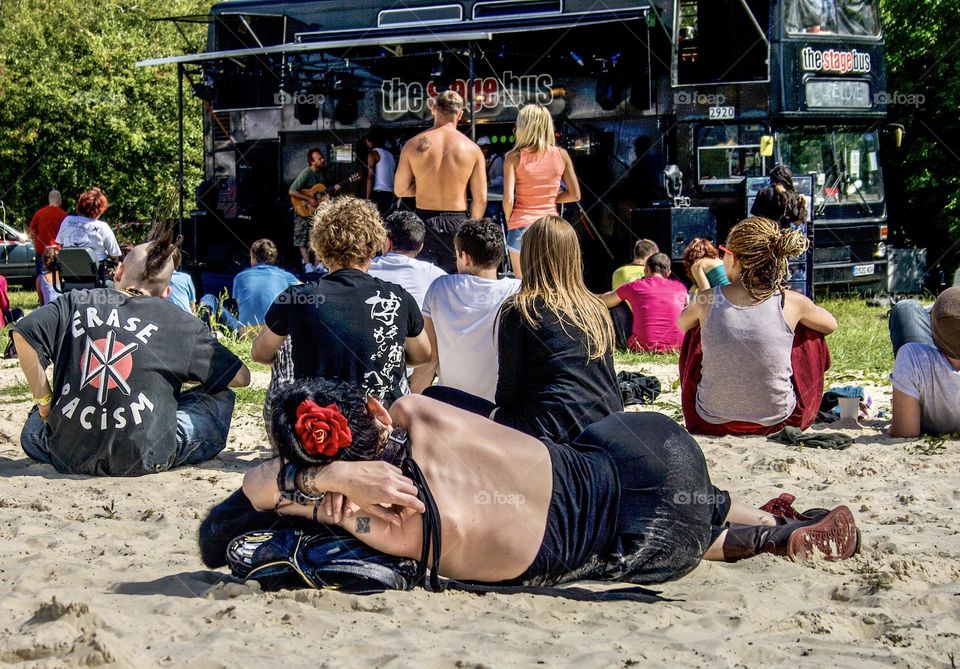 A crowd on people relax watching a band play on a stage at a summer festival 