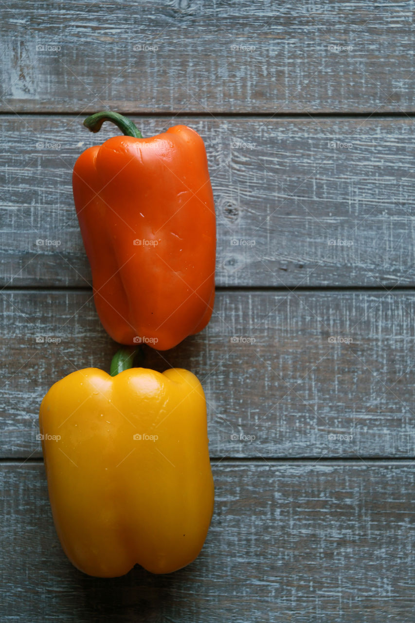 Sweet and tasty yellow and orange bell peppers sit in a flat lay on a wooden canvas board.