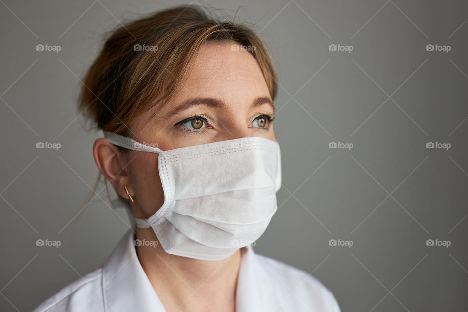 Doctor with face covered with mask. Portrait of young woman wearing the uniform, cap and mask to avoid virus infection and to prevent the spread of disease. Real people, authentic situations