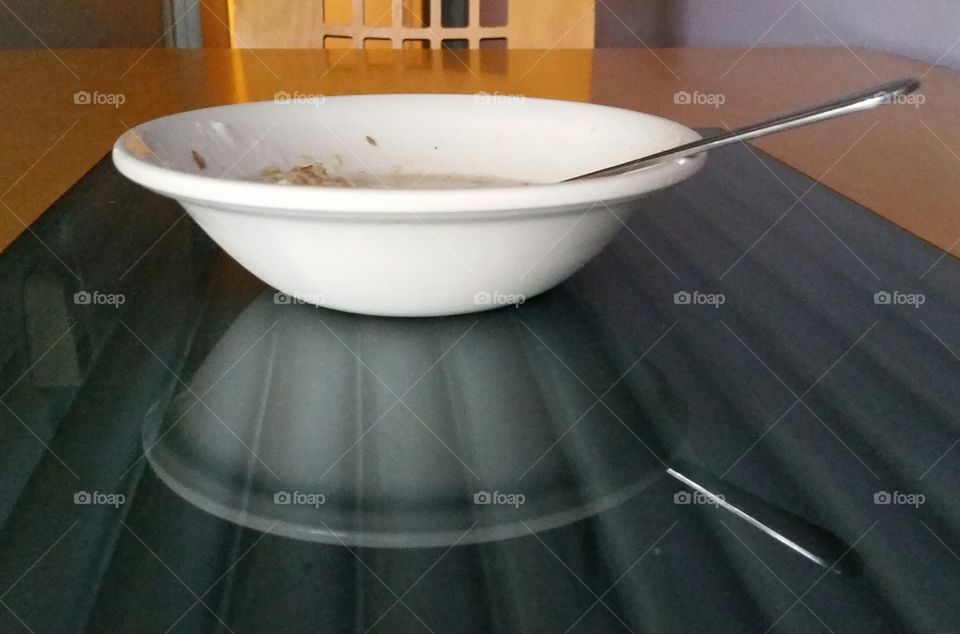 Reflection of  white cereal bowl and spoon at breakfast.