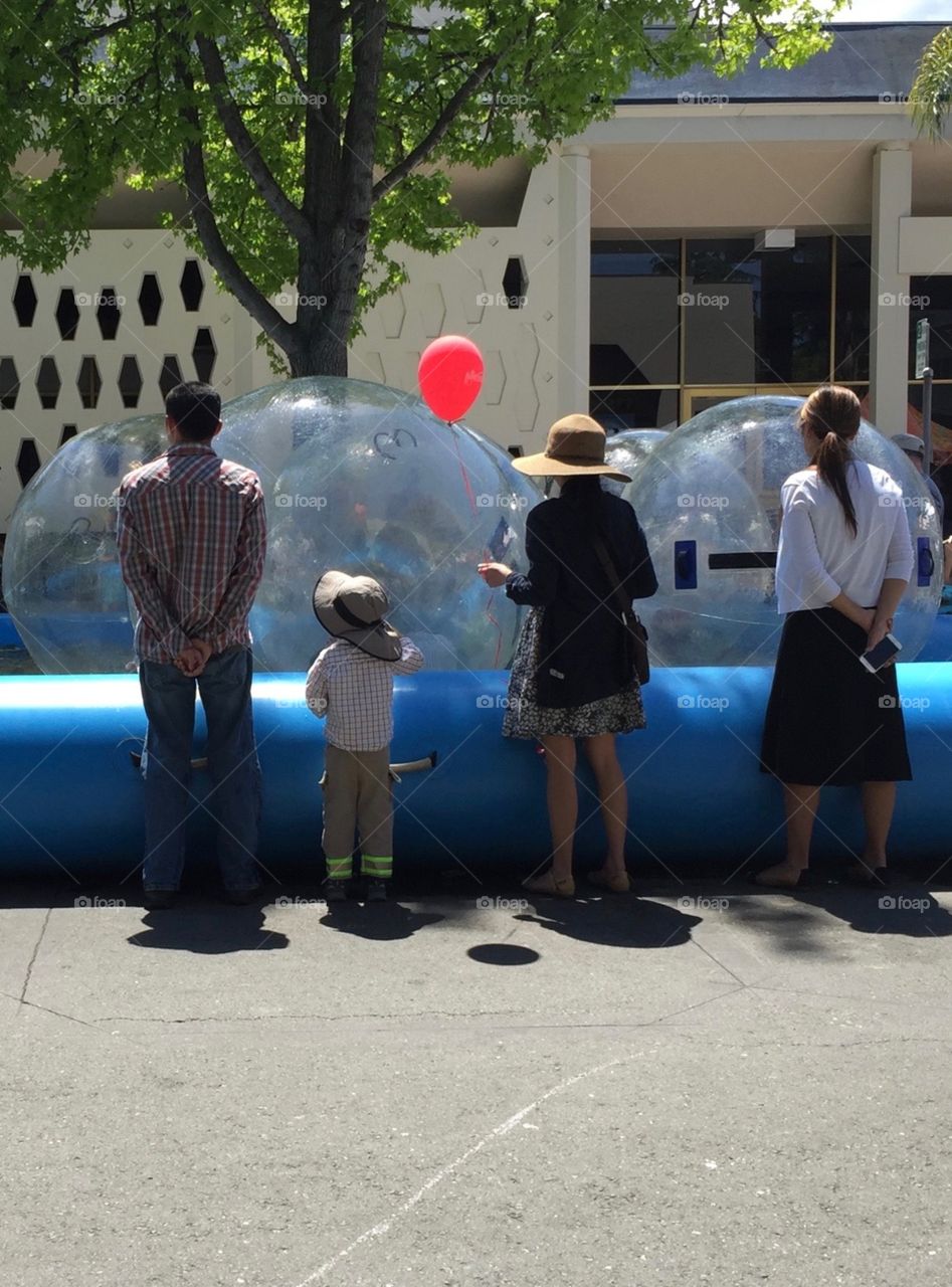 Family watching kids play inside big inflatable plastic transparent water rolling balls