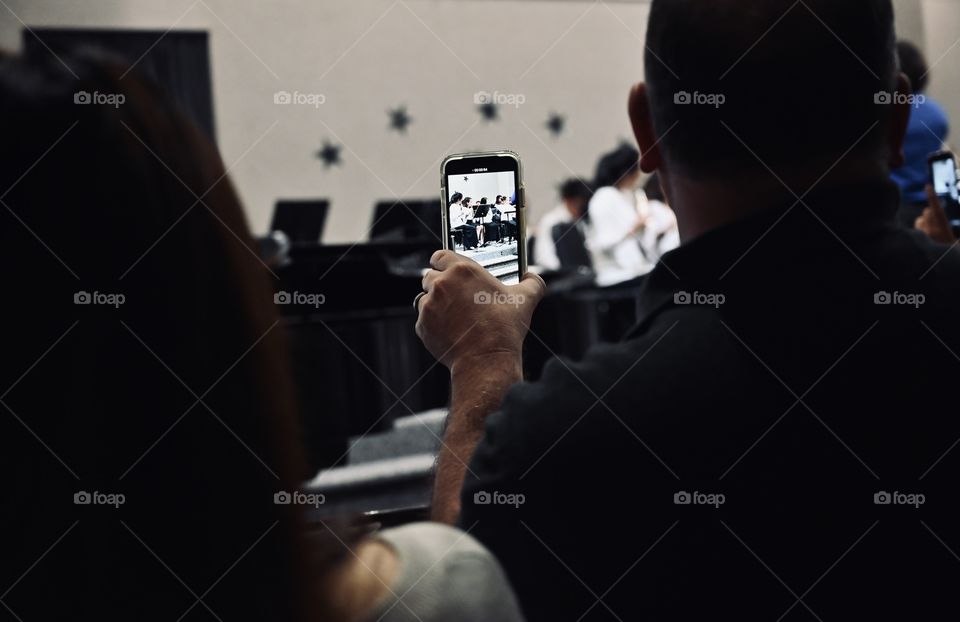 Proud parents who are watching their kid musical and capturing her through the phone.  