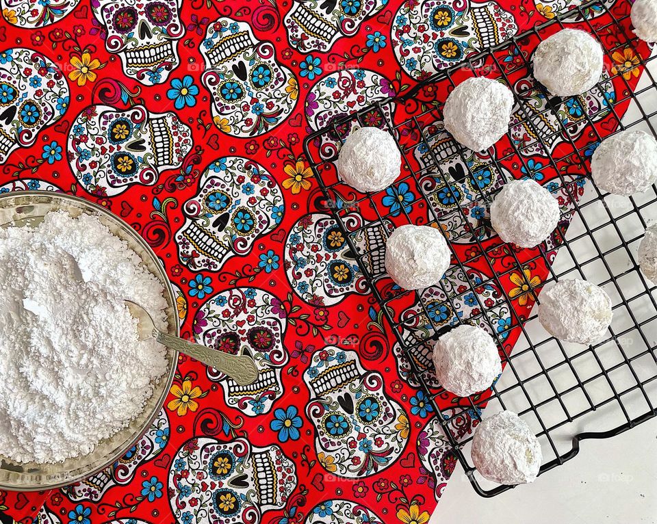 Placing Mexican wedding cookies on a cooling rack, rolling cookies in powdered sugar, making cookies at home, baking with toddlers, skull print with Mexican wedding cookies 