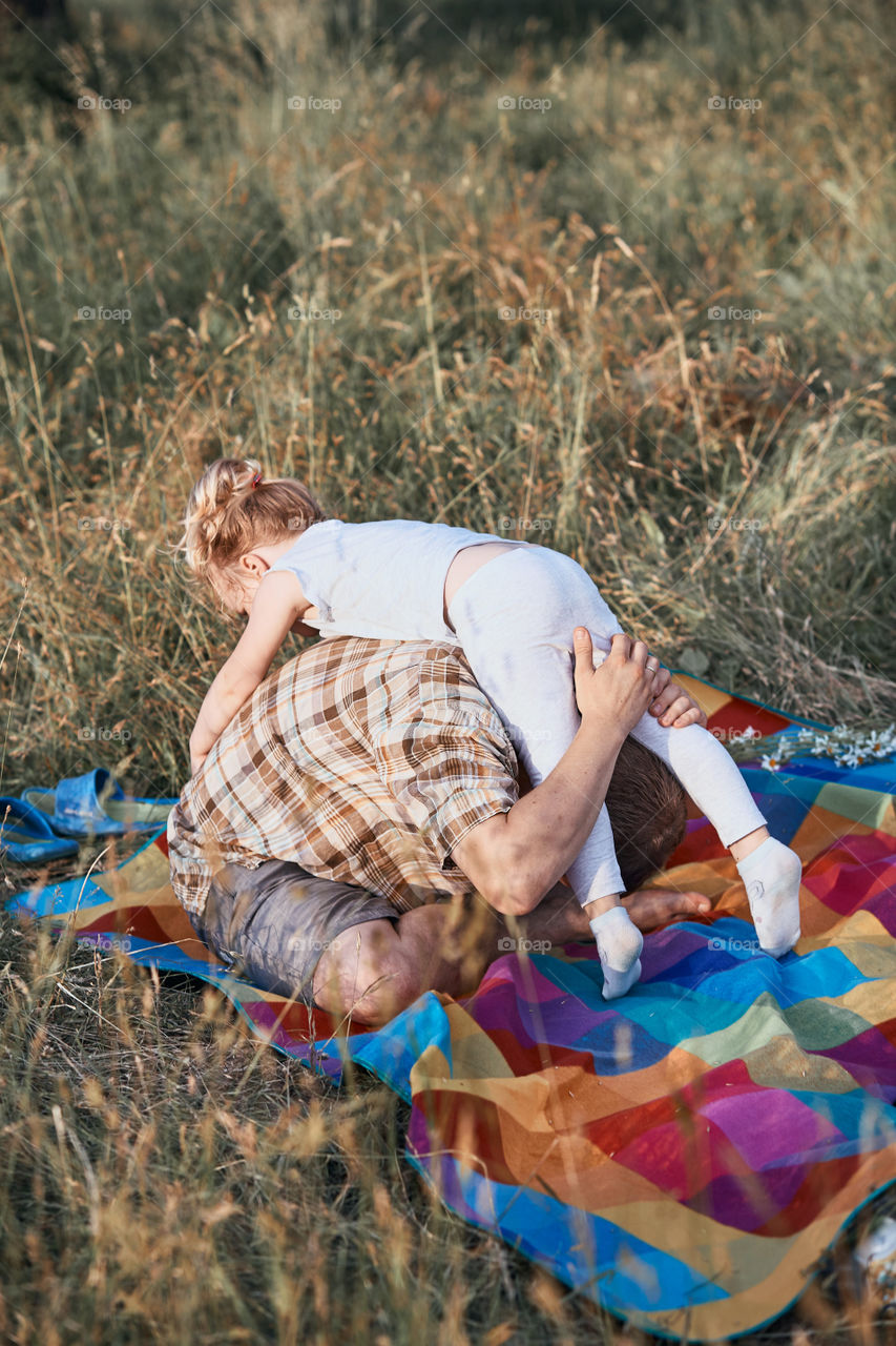 Father playing with little girl on a meadow, close to nature. Parents and children sitting and playing on a blanket on grass. Candid people, real moments, authentic situations