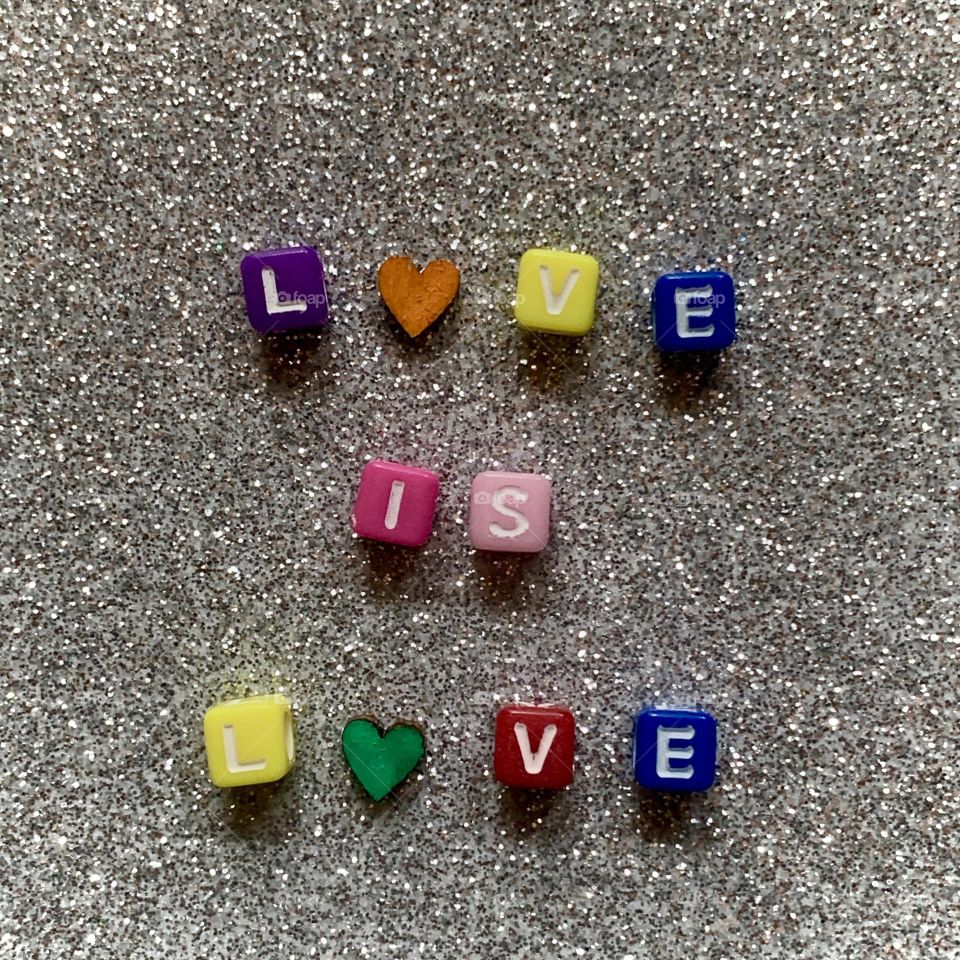 Love is Love spelled out with colourful lettering on a silver, glittery background 