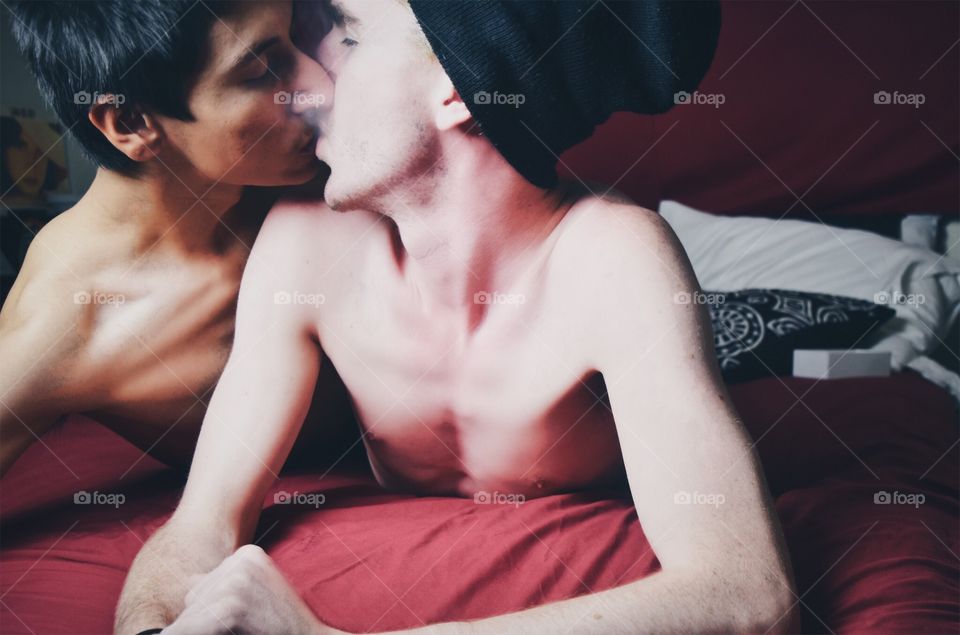 Two young men lie on a bed while in a loving embrace
