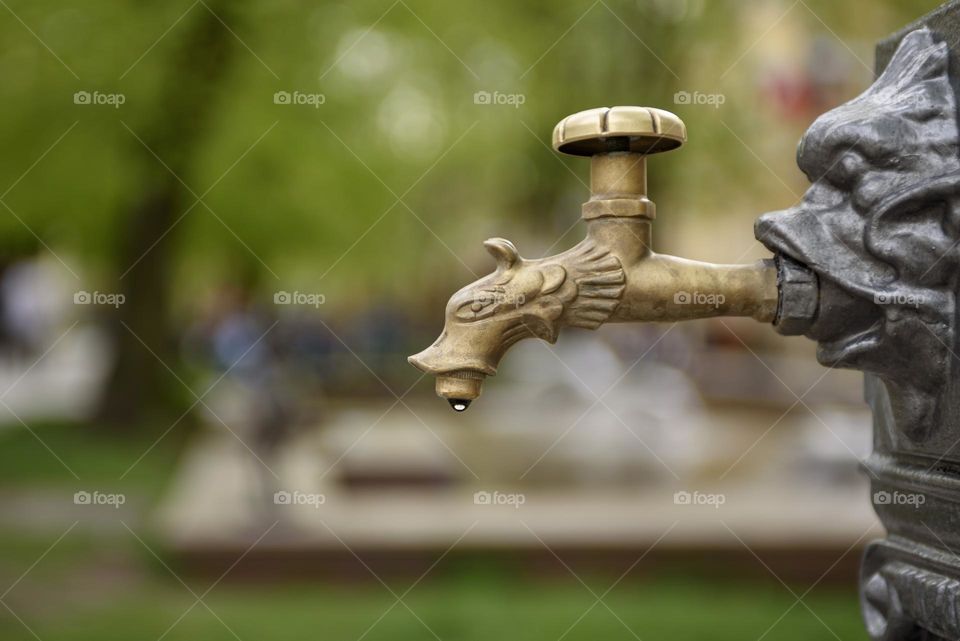 Antique iron faucet with a drop of water on a green background.