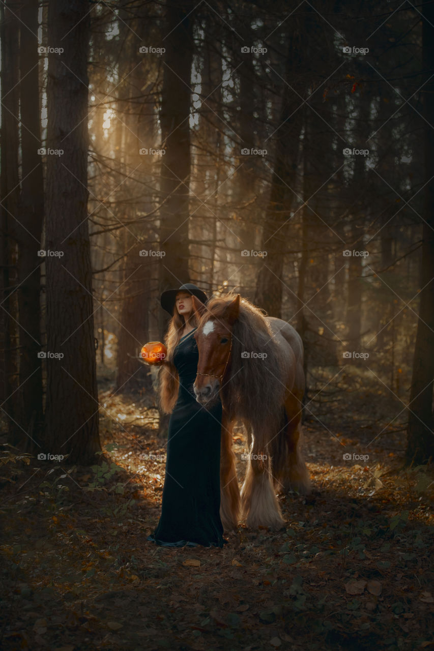 Woman in witch wear with horse in autumn park 