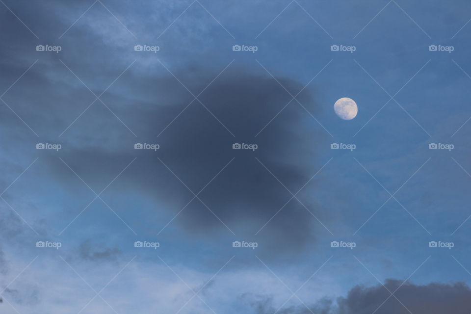 Waxing gibbous May moon with threatening dark clouds in blue sky 