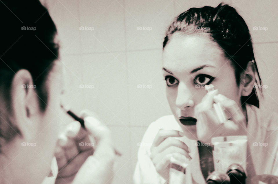 Reflection of woman applying eyeliner in mirror