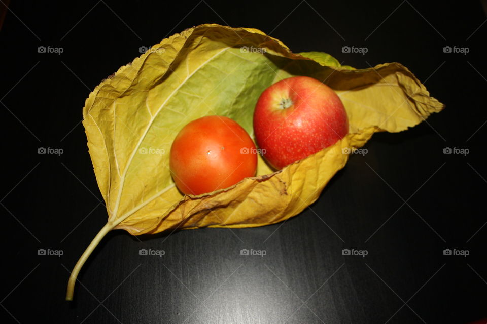 It is a large yellow autumn leaf. Inside the leaf I have put an apple and a tomato so that you can see how big the leaf is. The background is black.