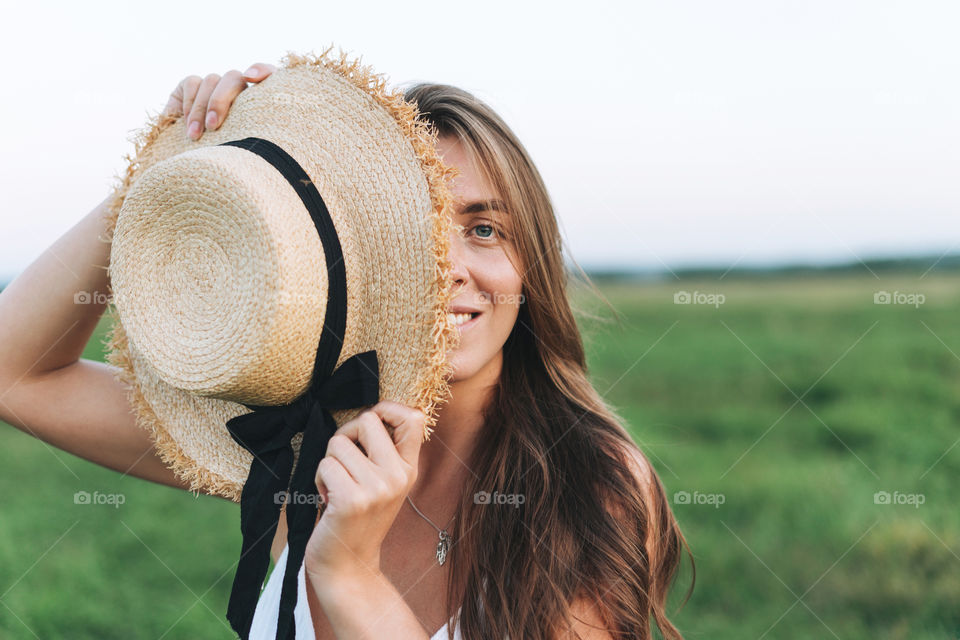 Young beautiful woman with hat near face on background of field 