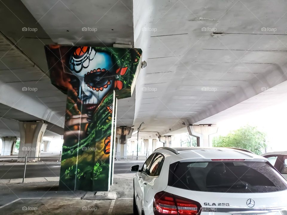 Visual street art on a cement highway pillar in a parking lot that celebrates Dia de los muertos/ Day of the dead.  A Mexican cultural tradition of celebrating and remembering those that have passed. Artist: @PauLGaris0n13