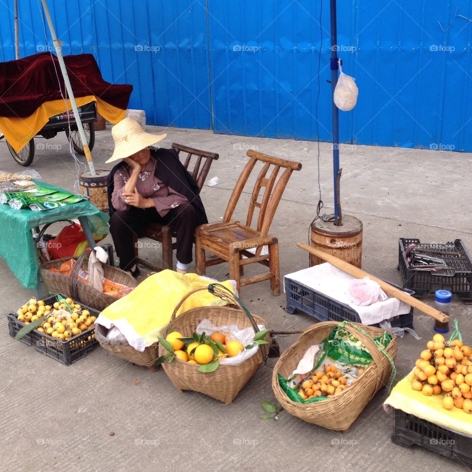 Slow Sales At The Fruit Stall. Chinese Woman Selling Fruit On The Street In China