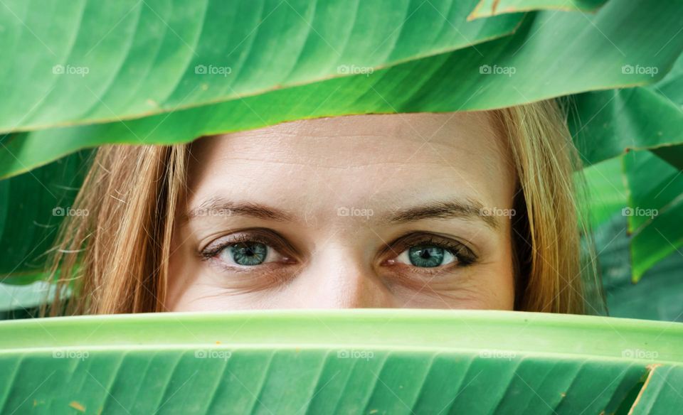 closeup woman eyes looking through palm leaves