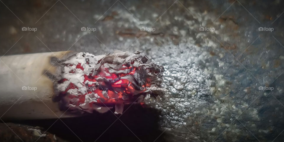 Cigarette burning against dirty background with tar to depict what it does to your lungs. Smoking kills.