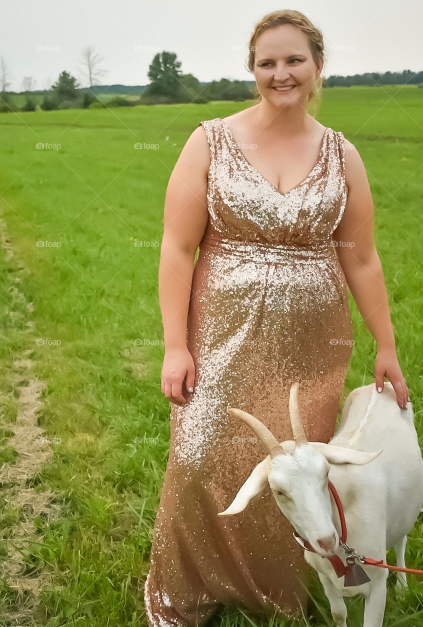 A plus size goddess bridesmaid in a rose gold sequin gown is laughing in a field, petting a goat. 