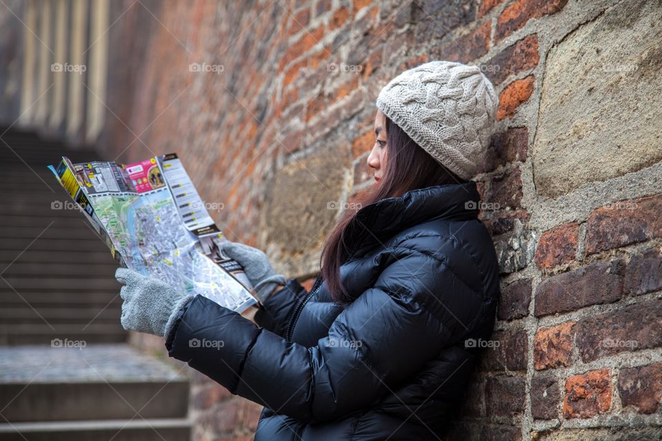 Woman reading map against brick wall