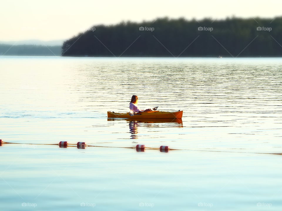 Woman in yellow kayak on calm lake in early morning