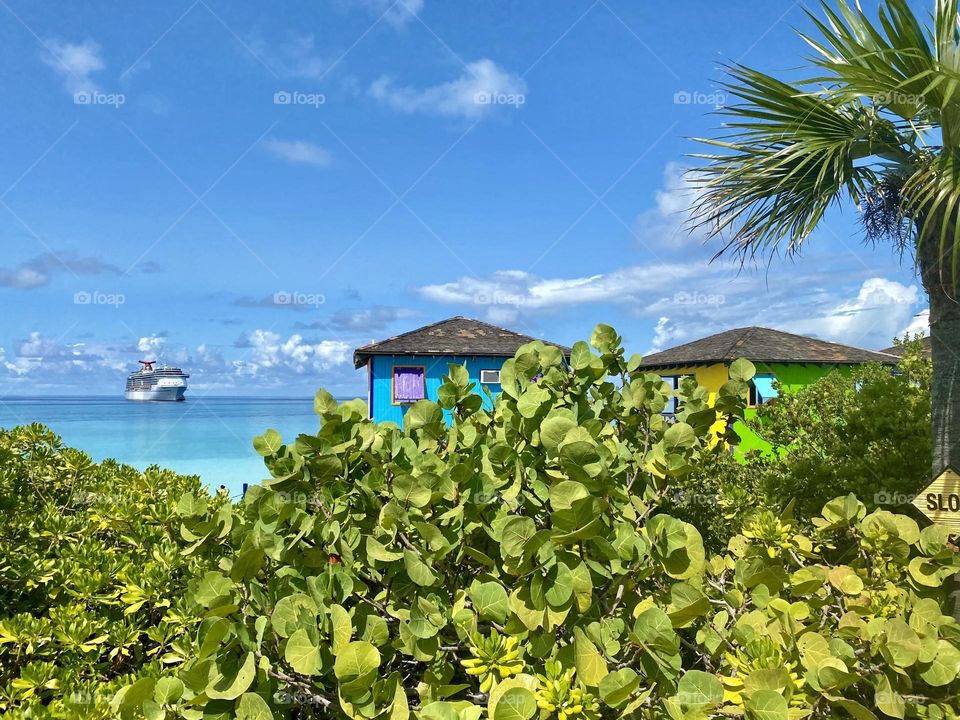 Two cabanas on the beach with a cruise ship in the background 