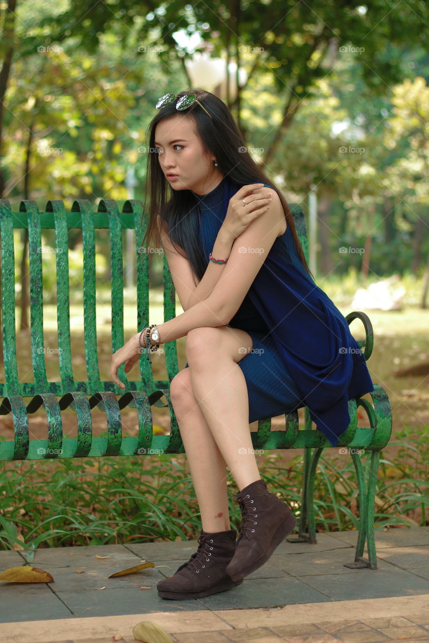 Asian woman sitting on metallic bench in park