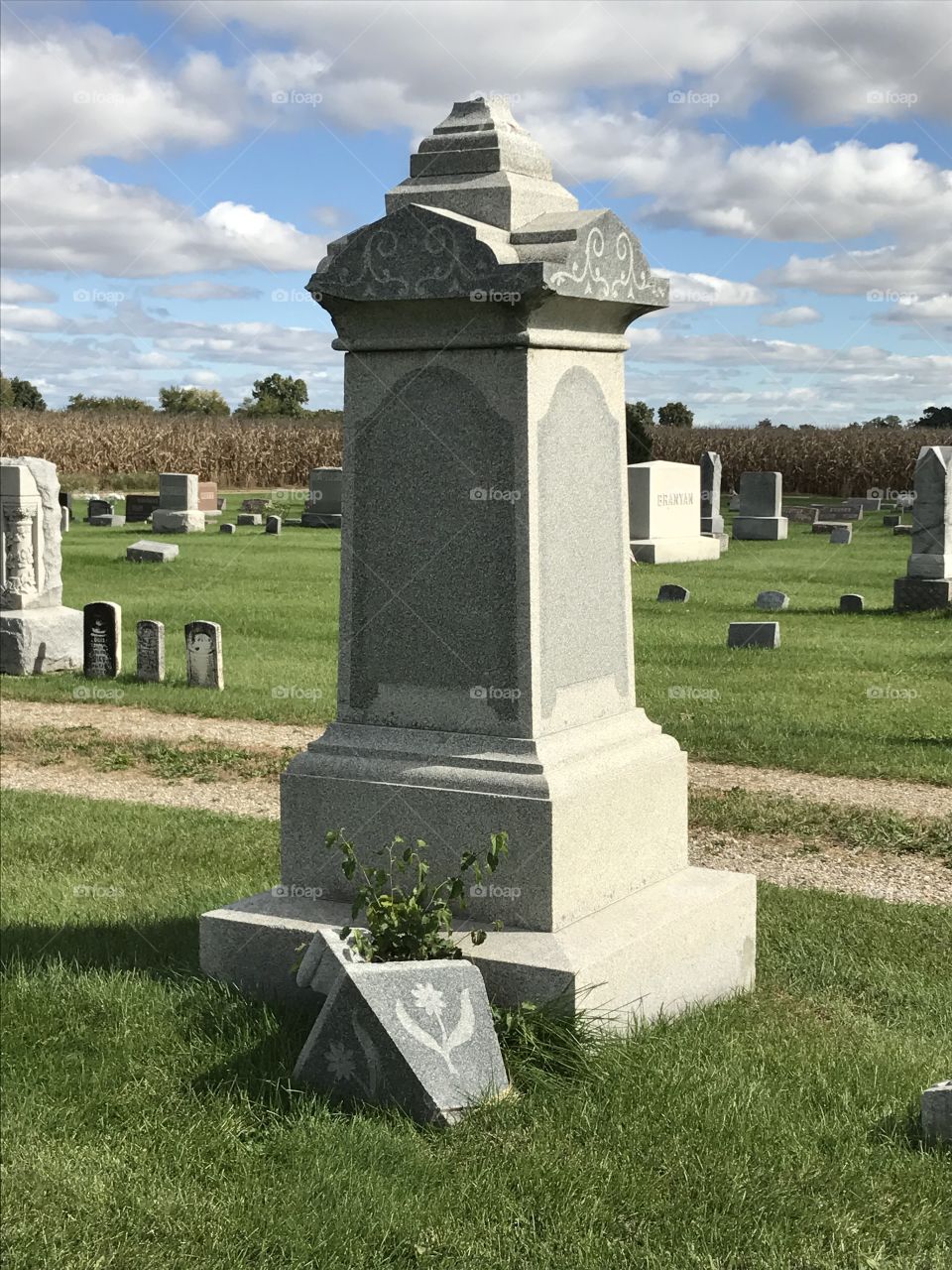 A monument with the top broken off and laying on the ground.