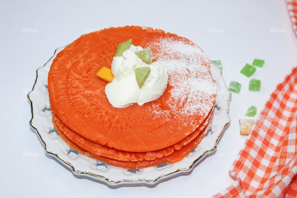 Orange pancakes with sour cream on a white plate,  on white table with white orange napkin.  Excellent breakfast