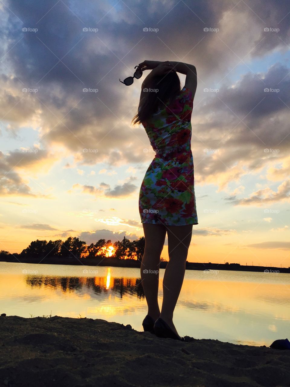 Rear view of young woman posing near lake at sunset