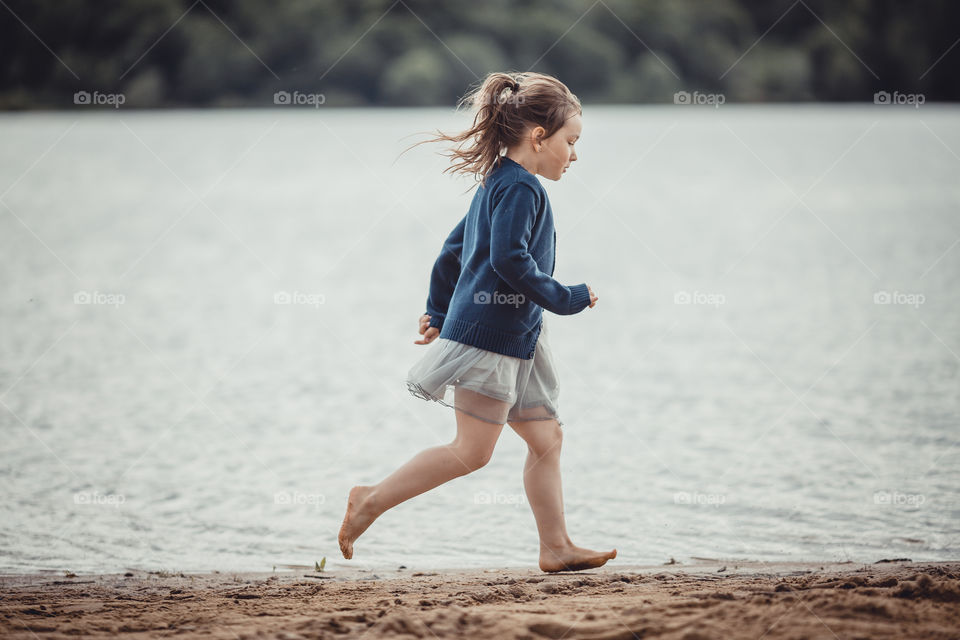 Little girl on lake coast at sunny evening. 