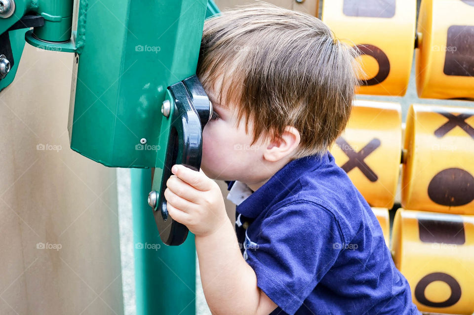 Young boy looking through a telescope on a playground at the park